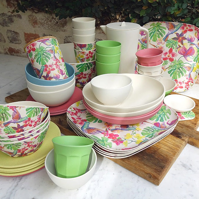 A bright and cheerful looking set of tableware comprising of floral patterned square plates and solid coloured bowls and cups in cream, melon pink, bright green and sea blue.